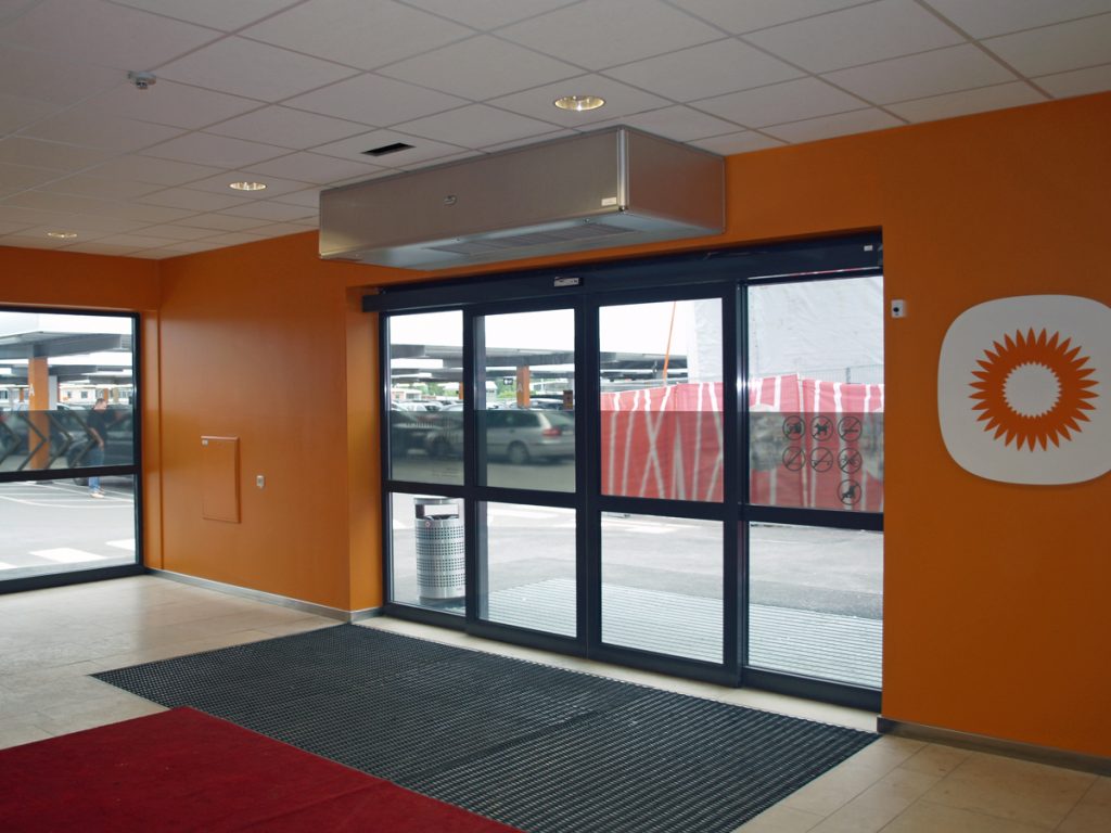 En ovanblåsande luftridå från RMK i en entré med orange vägg.