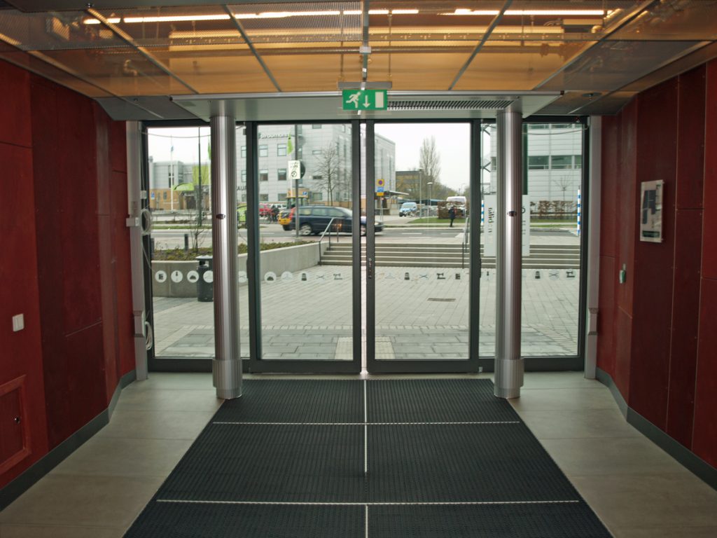 En sidoblåsande luftridå från RMK i en entré med röd vägg.