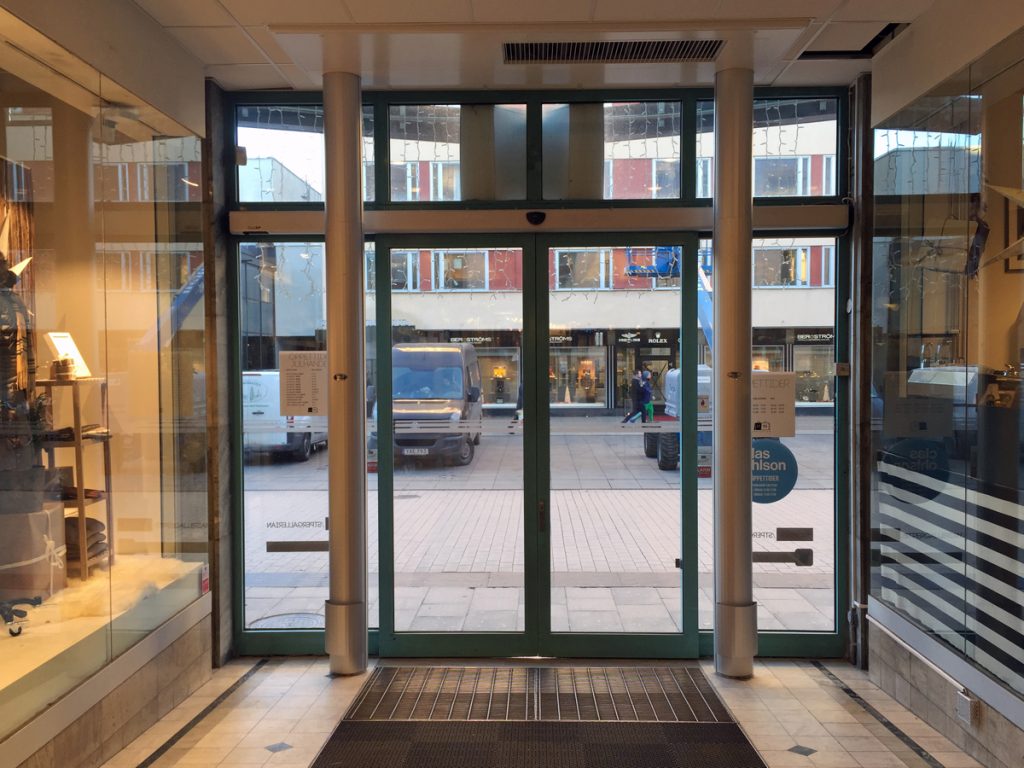 En sidoblåsande luftridå från RMK i en entré med gröna dörrar.