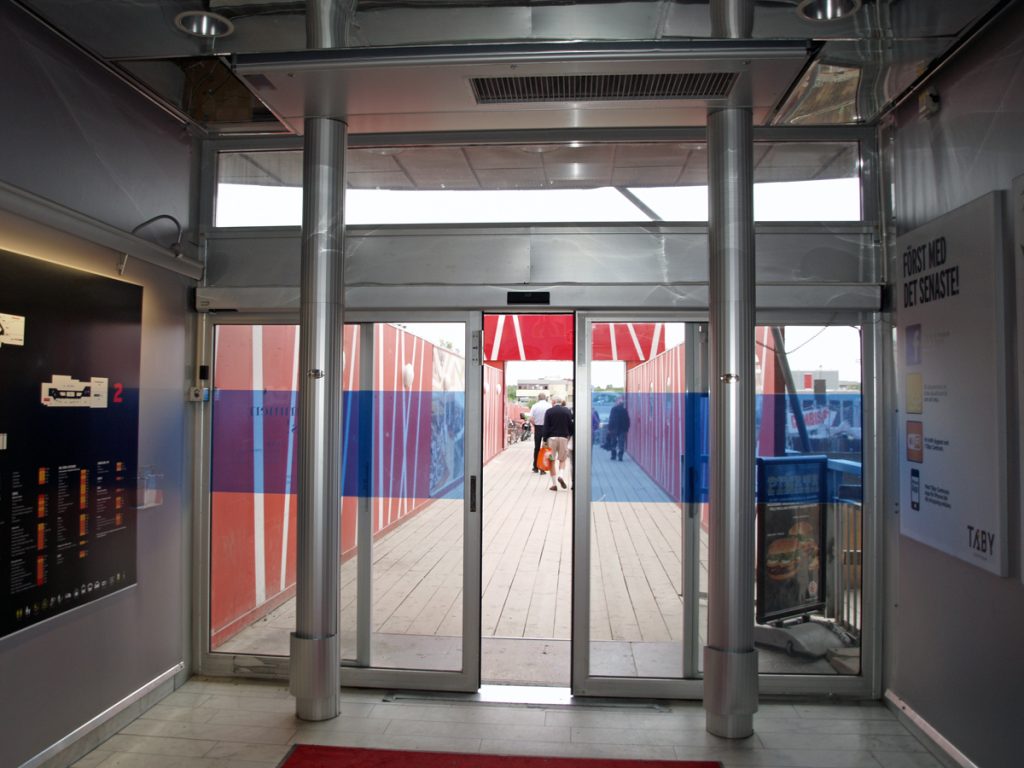 En sidoblåsande luftridå från RMK i en entré med röd vägg.