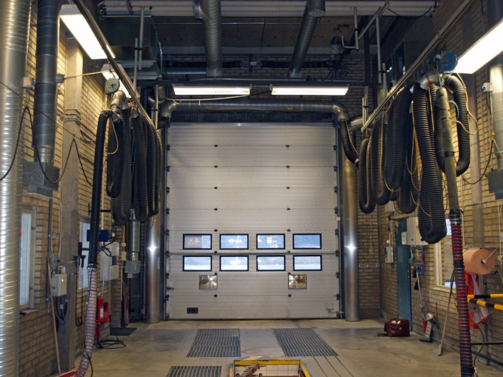 Sidoblåsande luftridåer från RMK på industriport på bilprovning med avgasslangar.