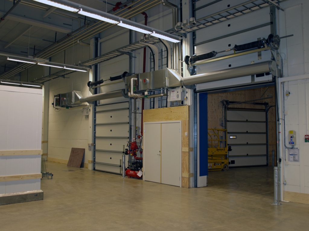 Ovanblåsande luftridåer från RMK på industriport med blå pelare.