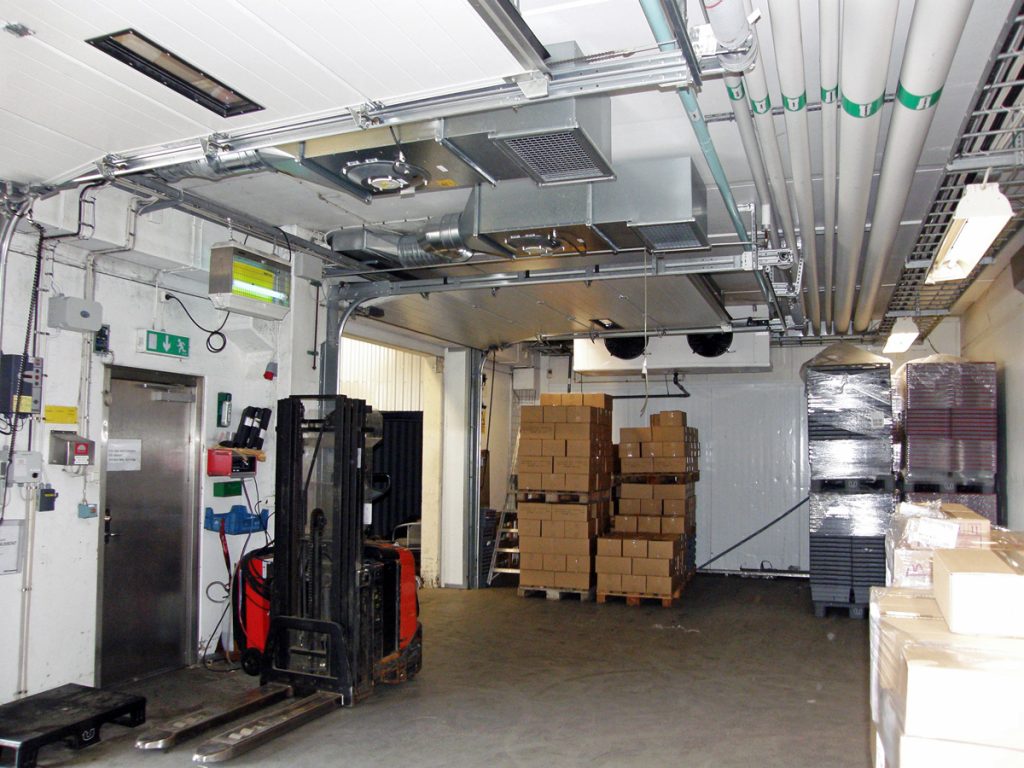 Ovanblåsande luftridåer från RMK på industriport med truck och lastpallar.