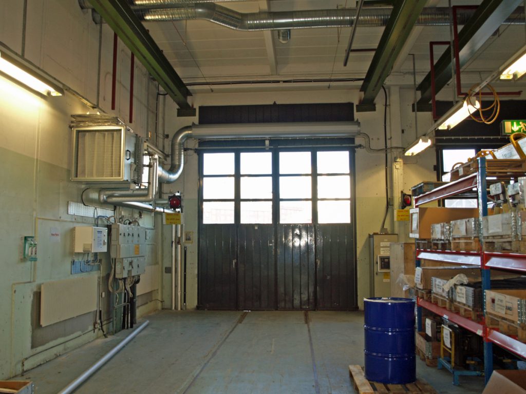 En ovanblåsande luftridå från RMK på industriport med blå tunna.