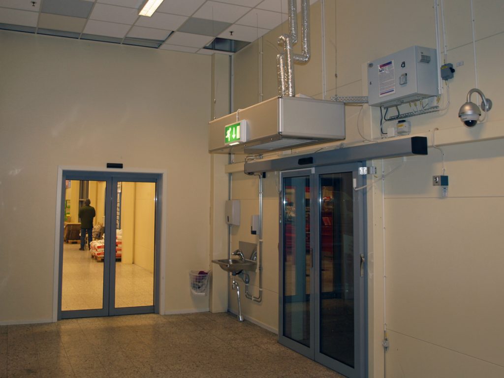 En ovanblåsande luftridå från RMK i en entré med beige vägg.