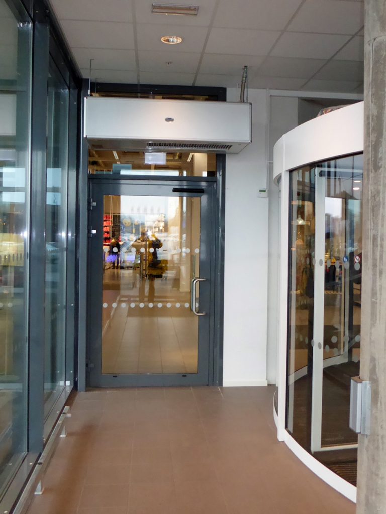En ovanblåsande luftridå från RMK i en entré med grå dörr.