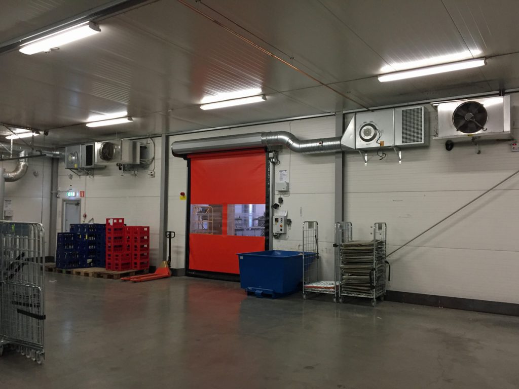 Ovanblåsande luftridå på ett kylrum med röd port.
